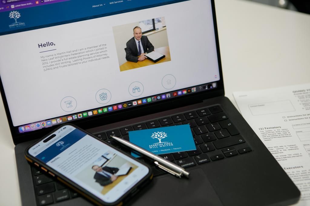 Laptop and phone displaying a website with a man in a suit. Business card and pen on the laptop.