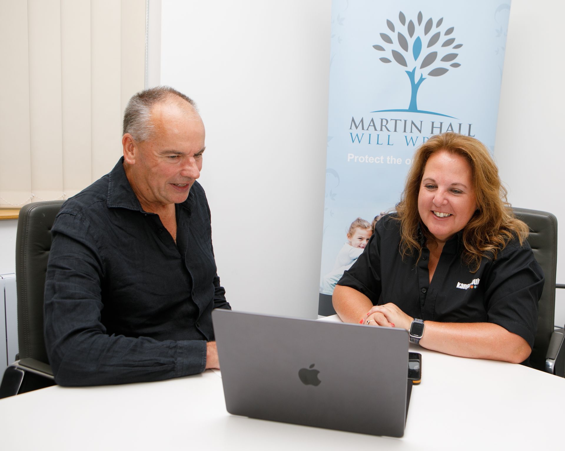 Two people looking at a laptop, inside a well-lit office, discussing documents.