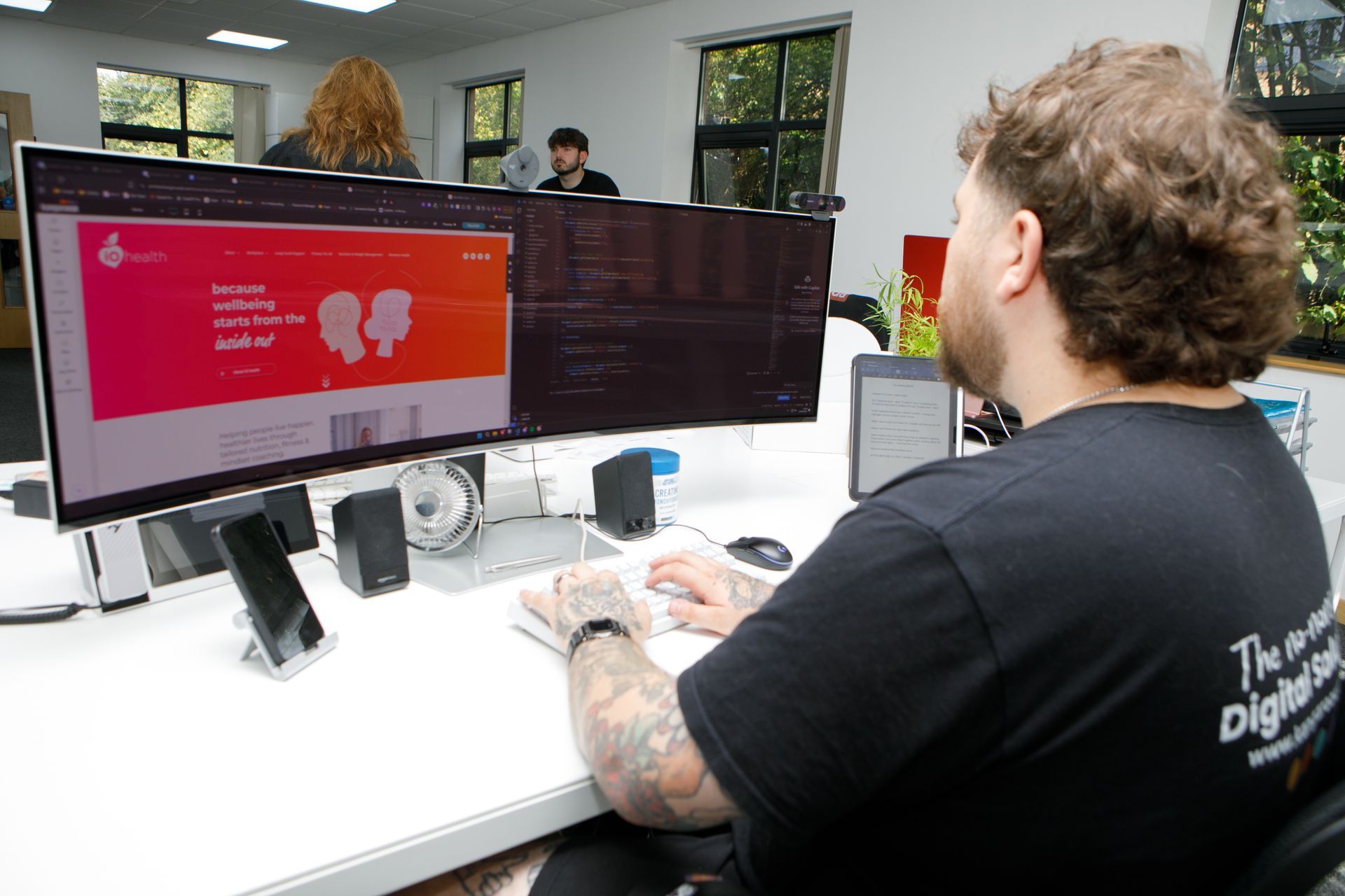 Person working at a desk with dual monitors displaying code in an office