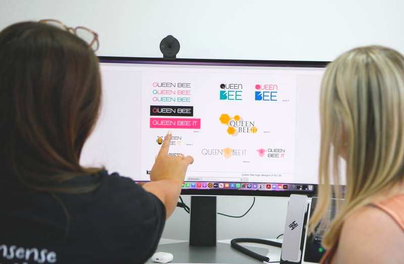 Two women reviewing logo designs on a computer screen; one points at the screen.