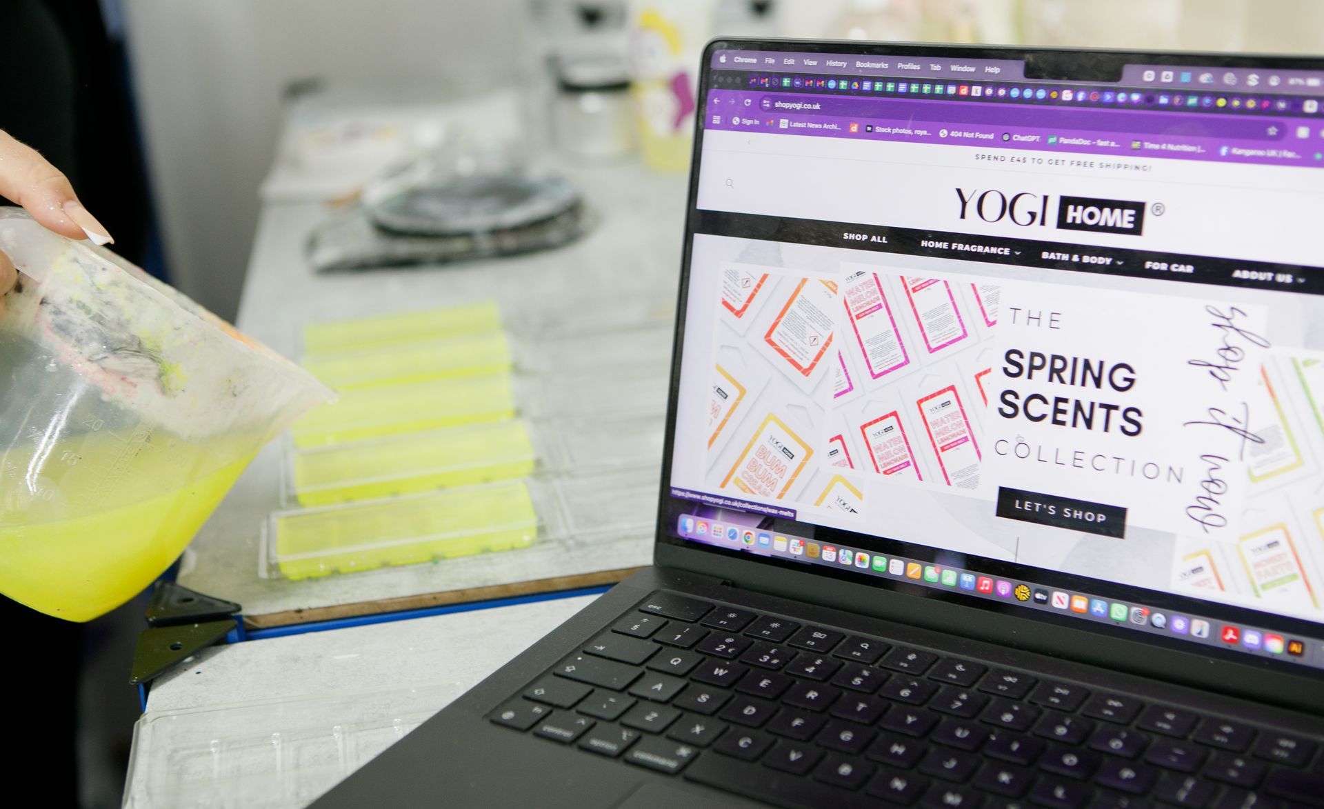 A person pours yellow liquid into wax melt molds next to a laptop displaying the Yogi Home Spring Scents collection.