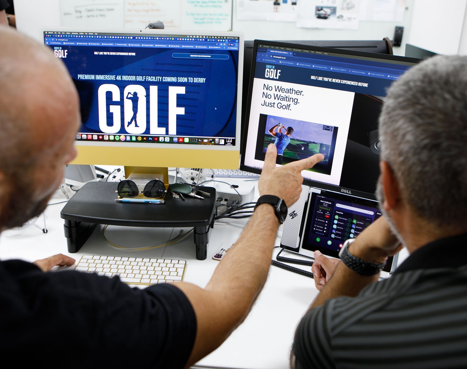 Two men at computers discussing a website about golf, one pointing at the screen.