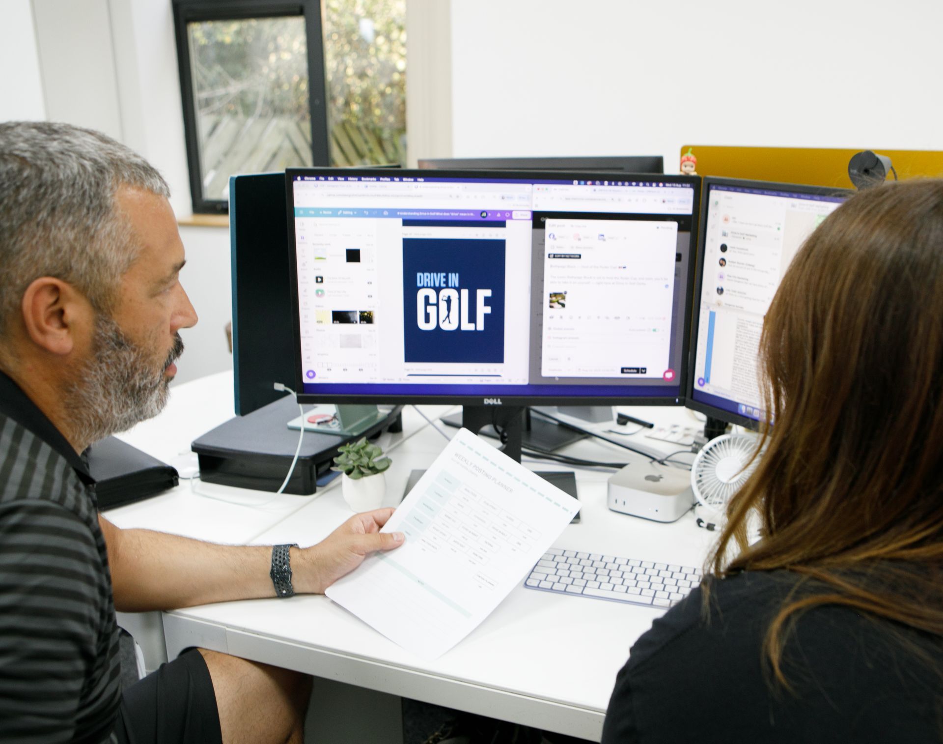 Man and woman reviewing content on a computer with multiple monitors in an office.