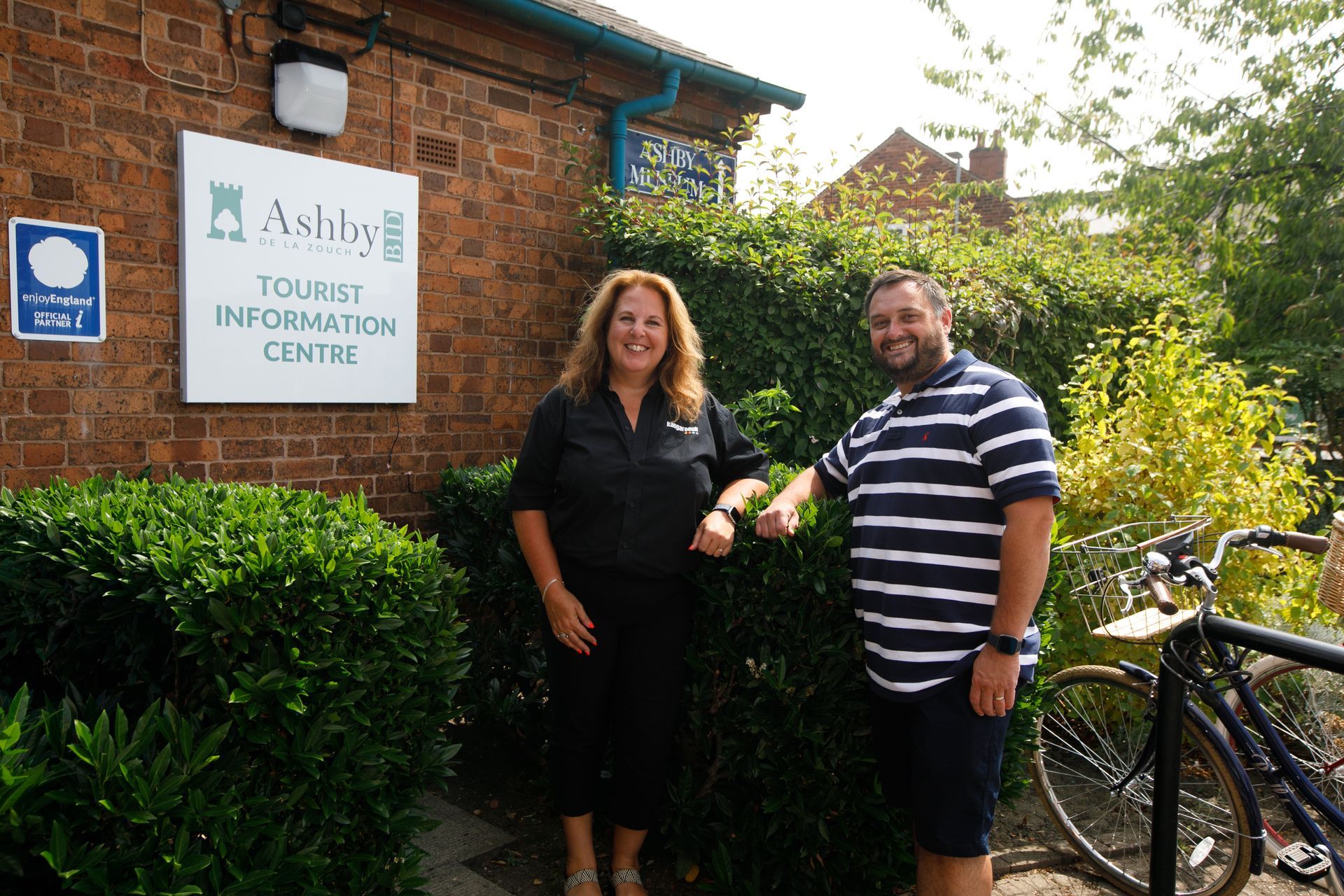 Two people, a man and a woman, standing in front of an Ashby Tourist Information Centre.