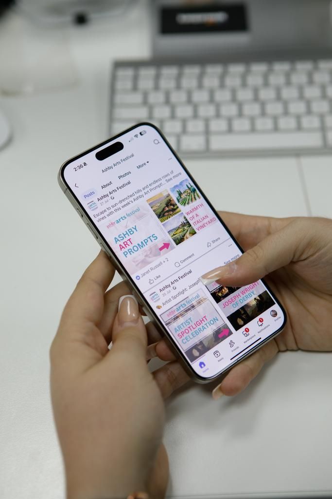 Hands holding a smartphone, scrolling through an app. White desk, keyboard in background.