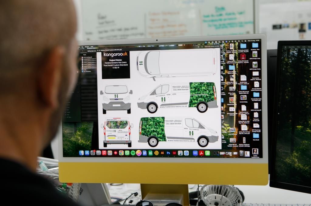 Man designing vehicle graphics on a computer. White van mockups with green camouflage detail.