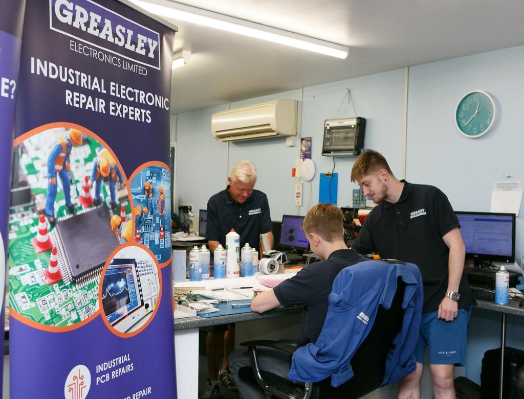 Men repairing industrial electronics in a workshop, banner says