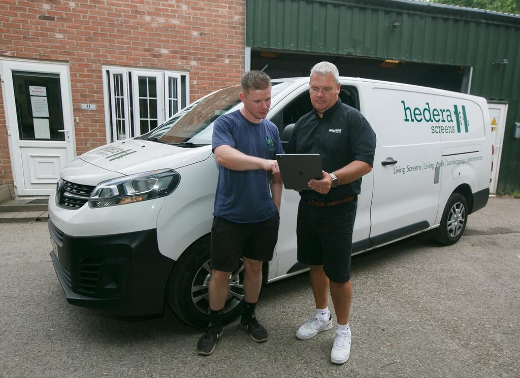 Two men beside a white van with company logo; one points at a tablet.