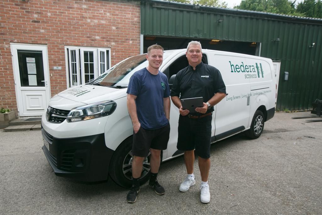 Two men stand next to a white van with company logo in front of a brick building.