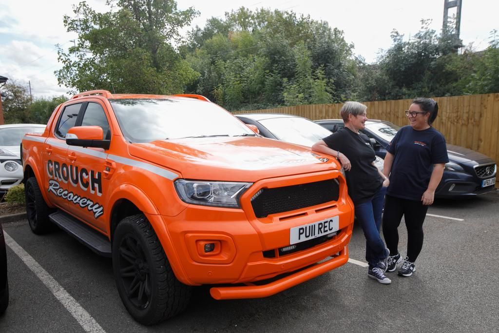 Two women standing next to a bright orange pickup truck with
