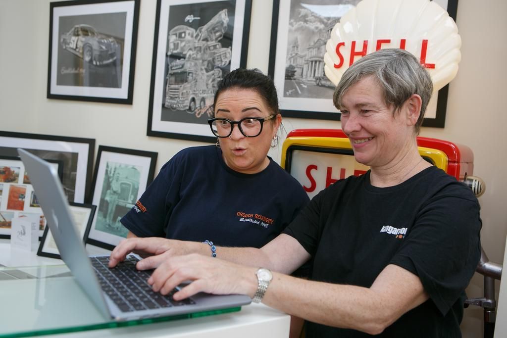 Two people look at a laptop screen together in an office decorated with vintage Shell signs and framed prints.