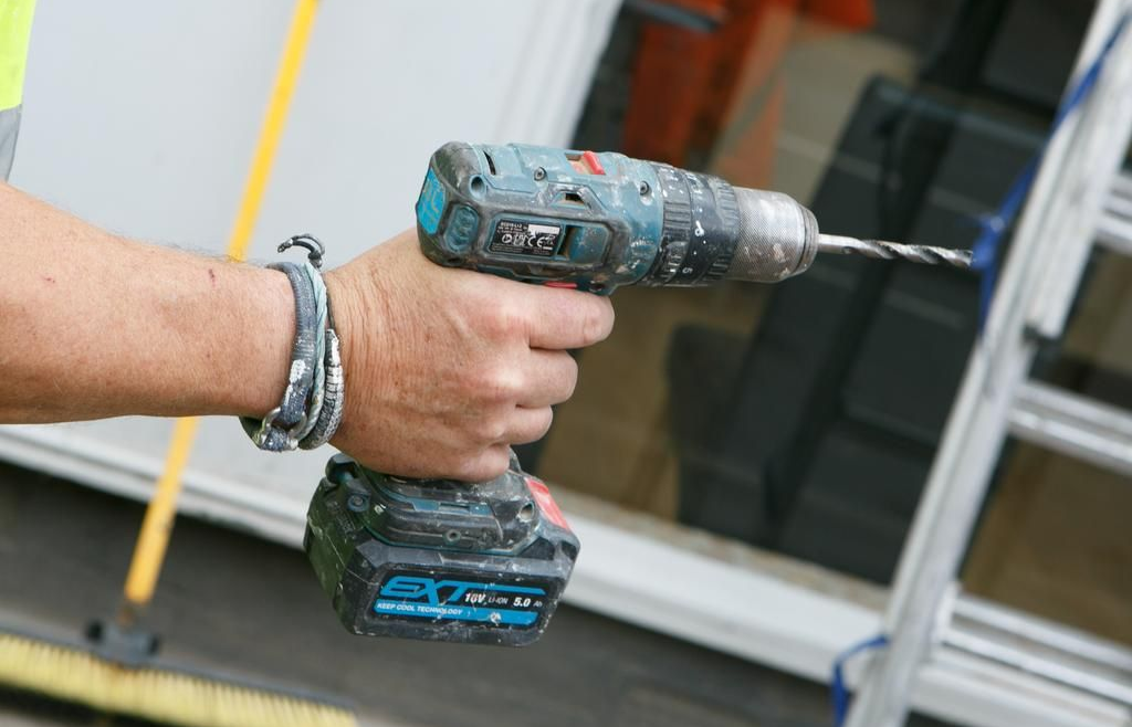 Hand holding a cordless drill, drilling near a window.