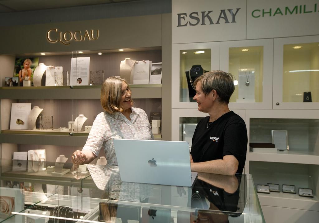 Two people chatting behind a glass display in a luxury eyewear store with designer frames on the shelves.