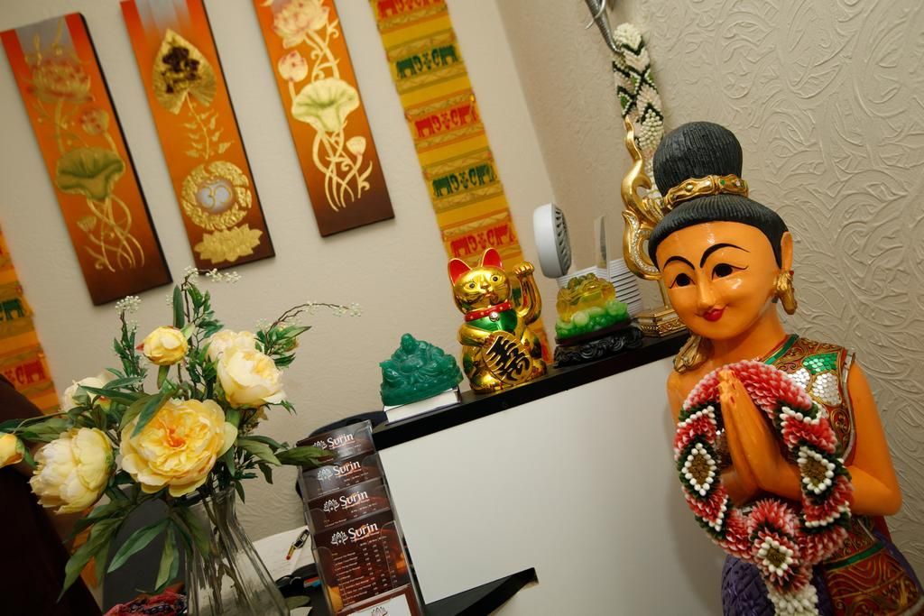 Statue of woman in prayer pose, flowers and art on wall, gold and colorful accents.