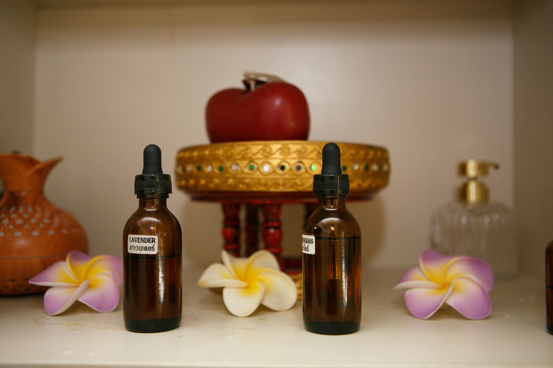 Bottles of essential oils with dropper tops, flowers, and a decorative apple on a shelf.