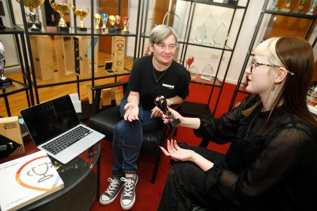 Woman sitting at a desk in front of a computer screen displaying a website. She smiles, with brown hair, and a watch.
