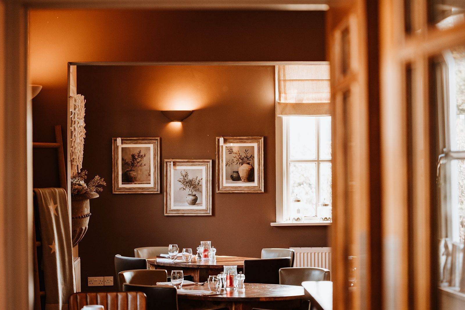 Restaurant interior with framed artwork, tables, and a window, warm colors.