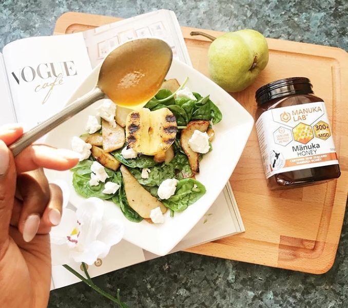 Woman pouring honey from a spoon over pear slices on a salad, with a jar of honey nearby.