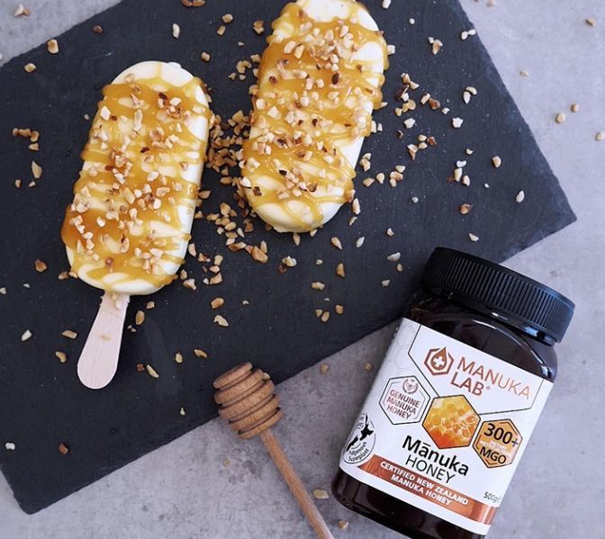 Two ice cream bars drizzled with caramel and nuts on a slate board, Manuka honey jar, honey dipper.