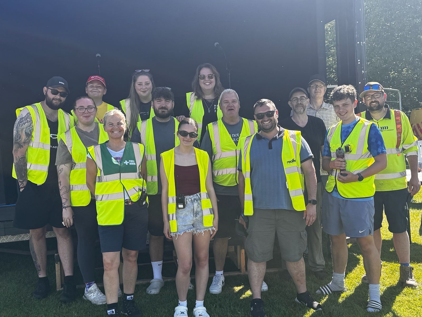 Team of volunteers in high-visibility yellow vests posing outdoors in front of the stage