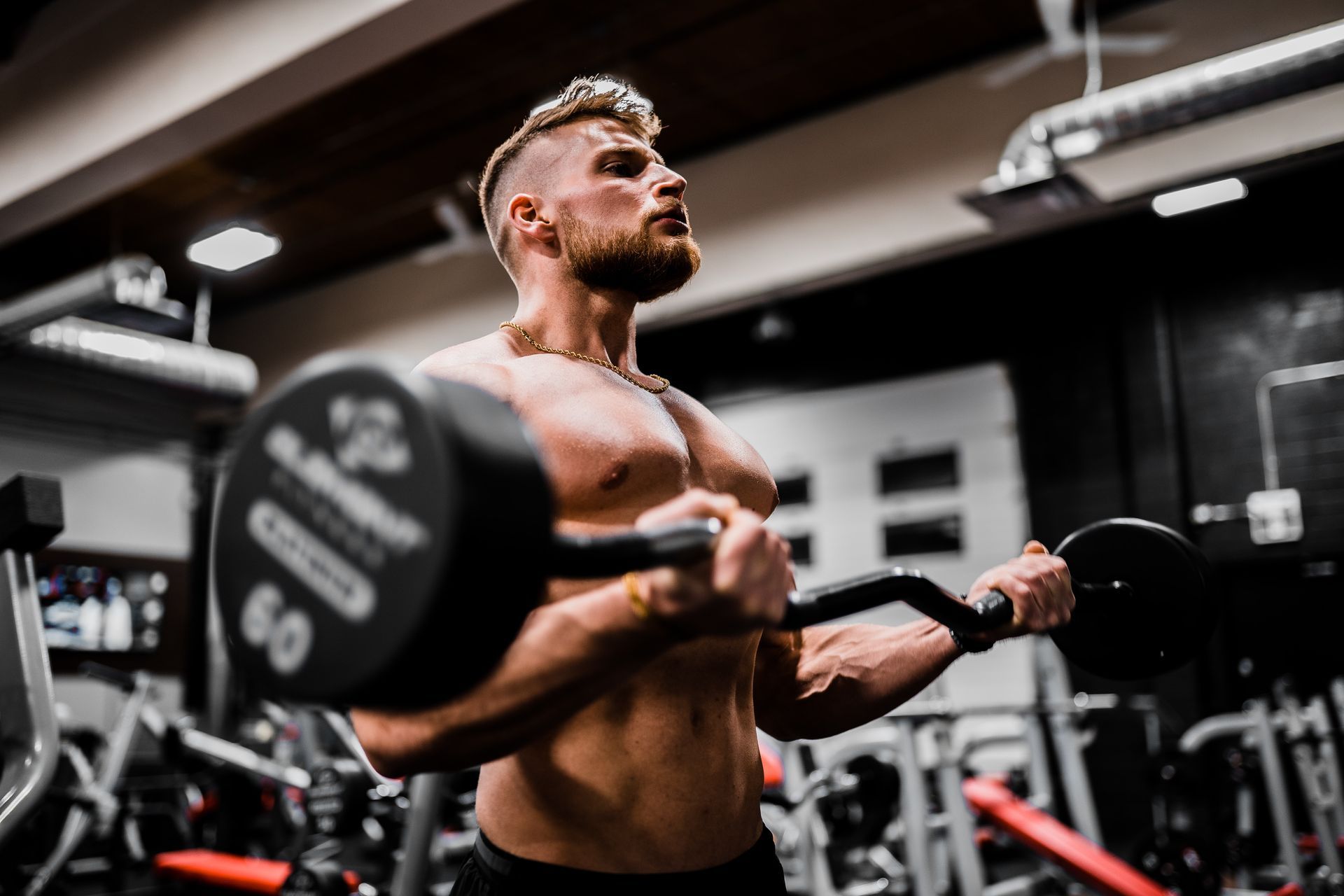 Man with a muscular build lifting a weighted barbell in a gym, focused expression.