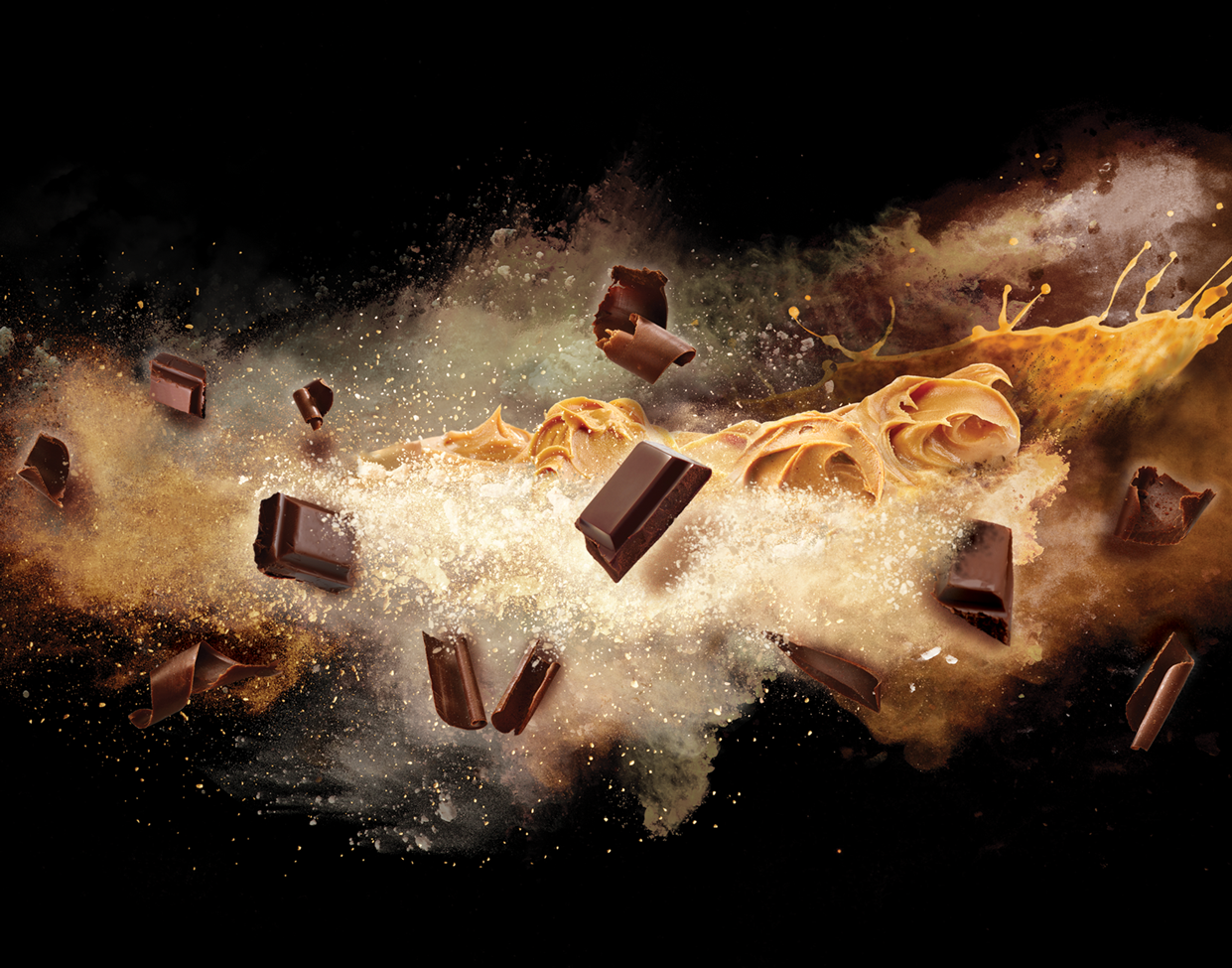 Dark chocolate chunks and smooth peanut butter swirl amid an explosive, dusty burst of ingredients against black.