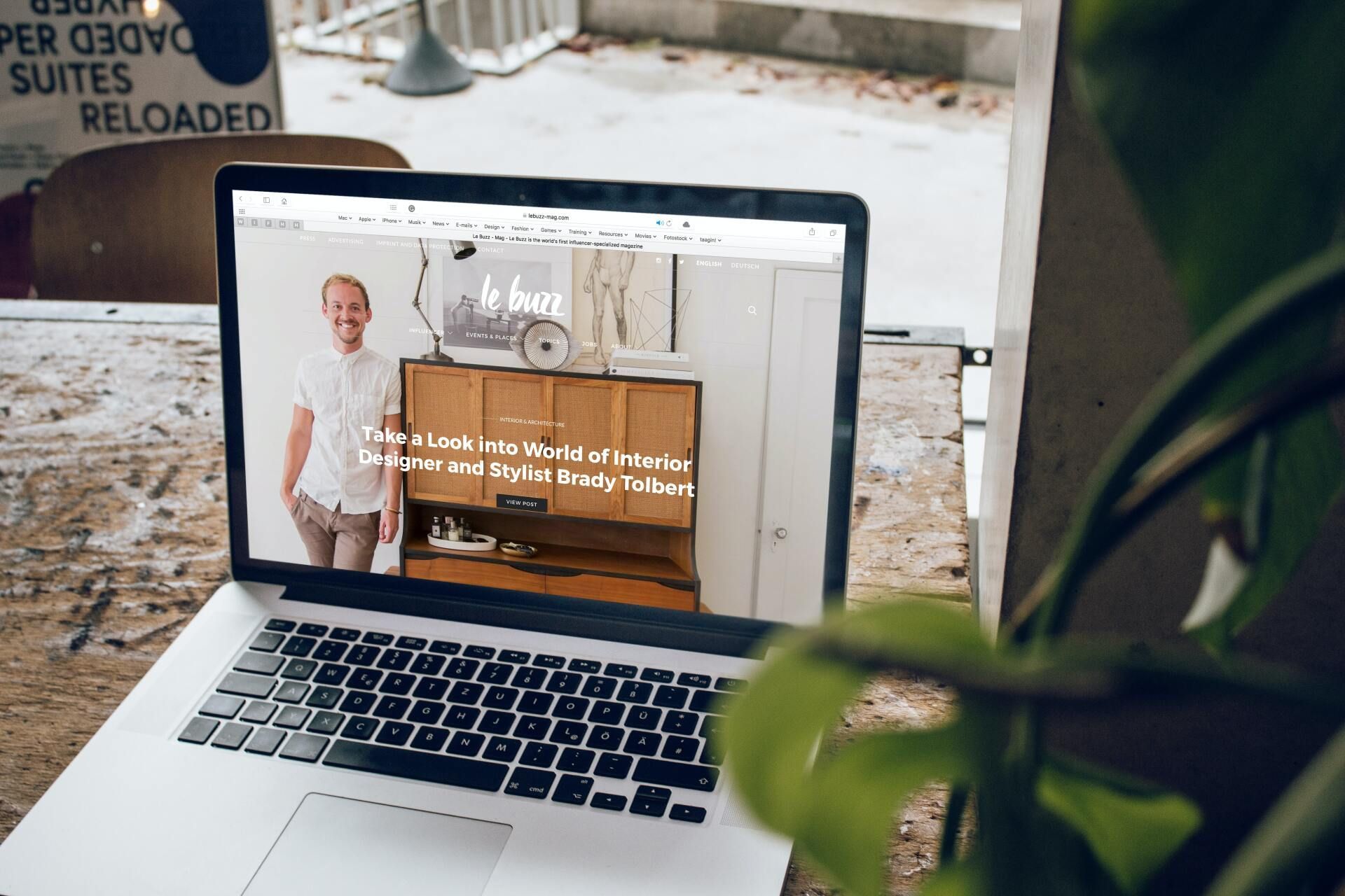 Laptop showing a website with a smiling man in a white shirt, on an outdoor table.