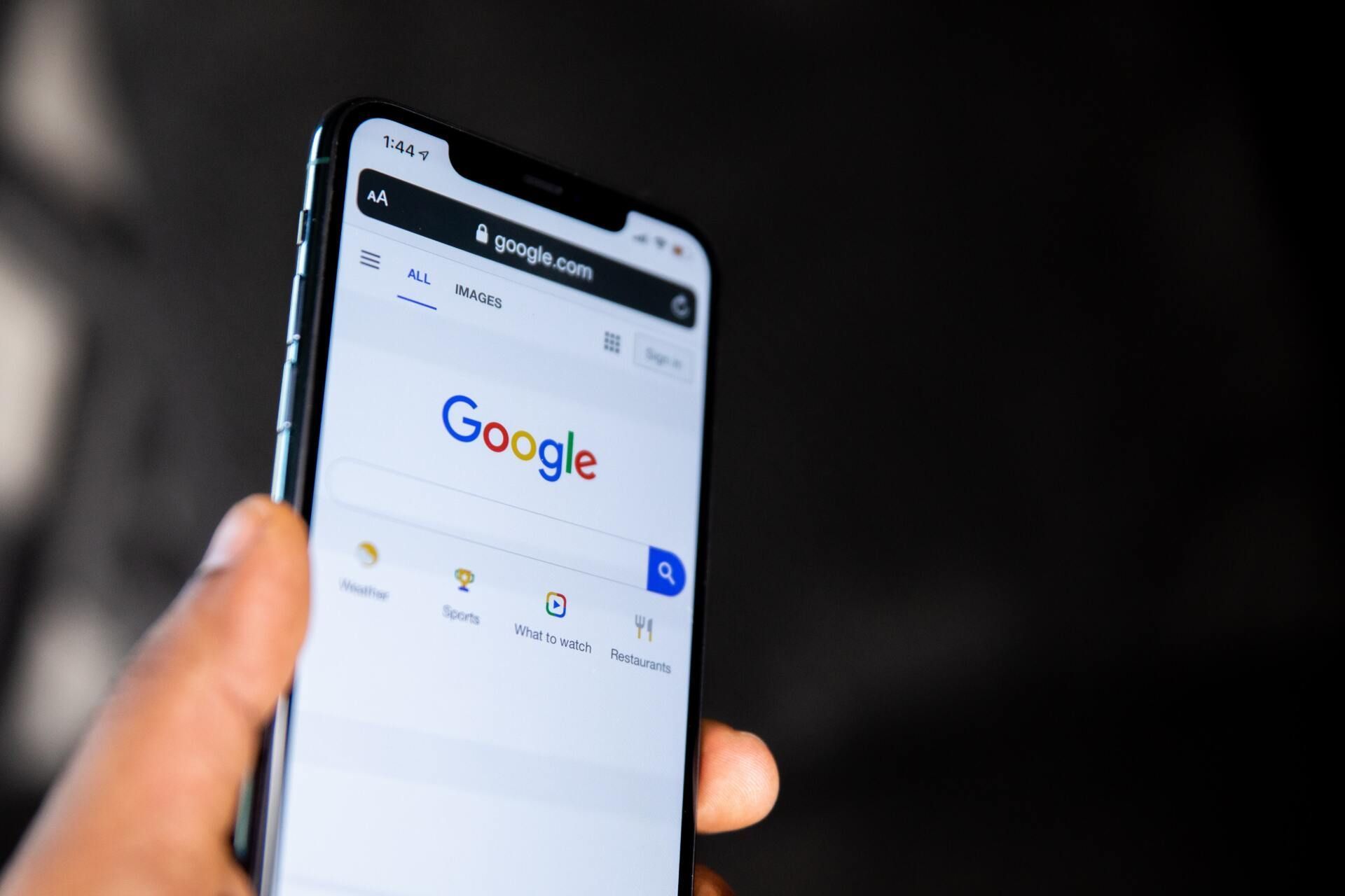 Hand holding a smartphone displaying the Google search page.