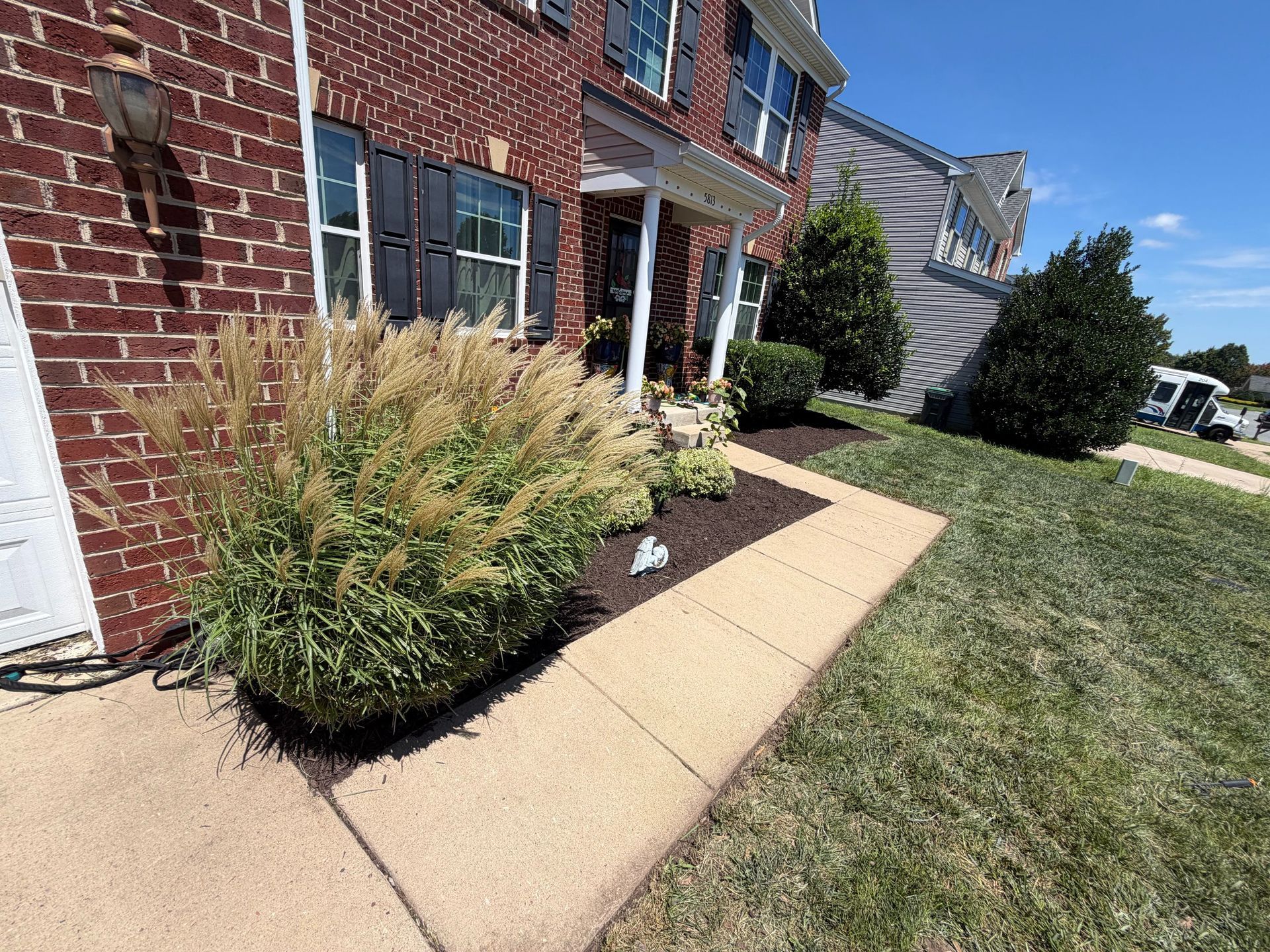 Brick house front walkway with tan pavers, landscaping, and lawn