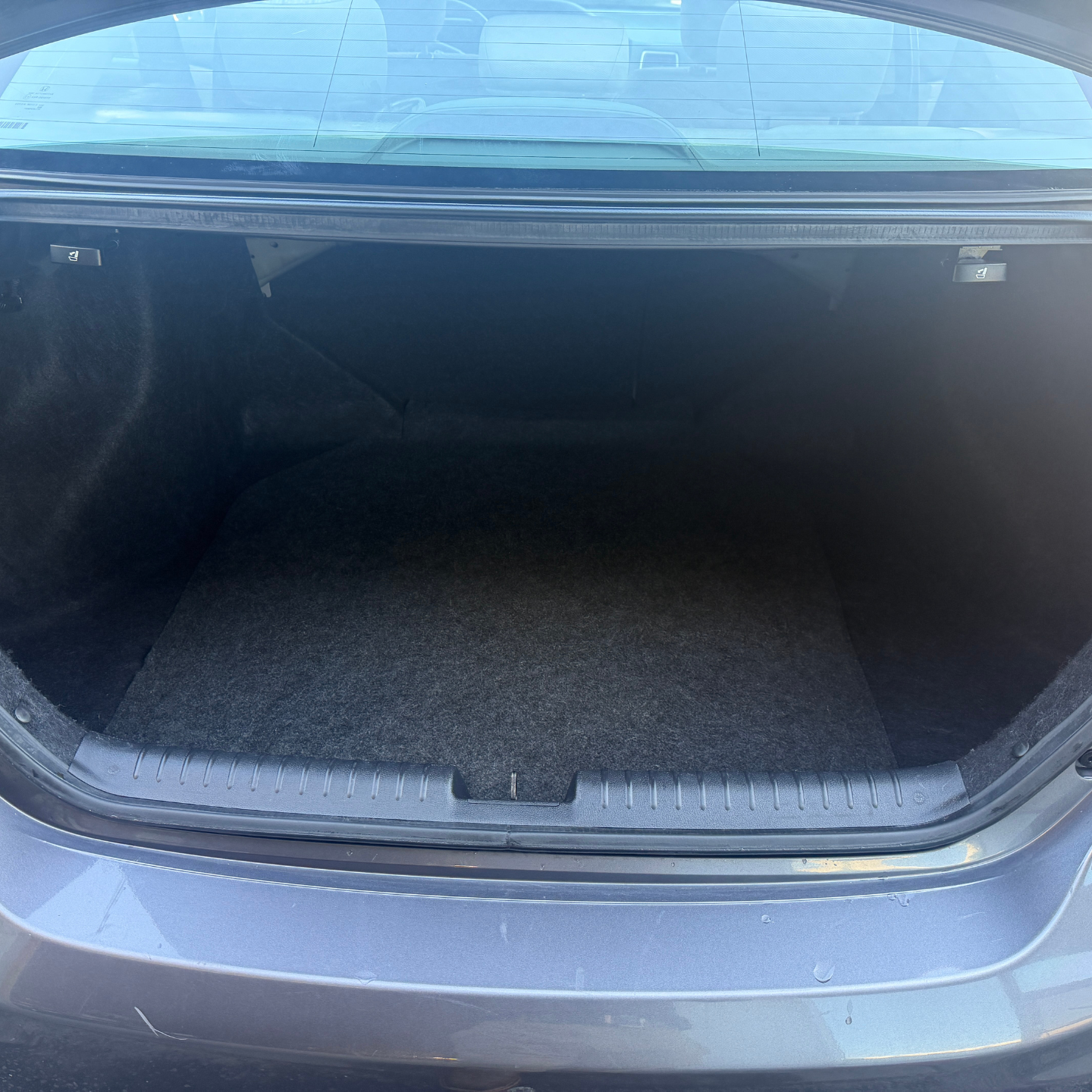 Open car trunk with dark cargo space and gray bumper