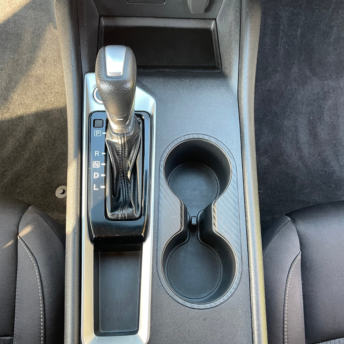 Car gear shifter beside a double cup holder and stitched center console trim