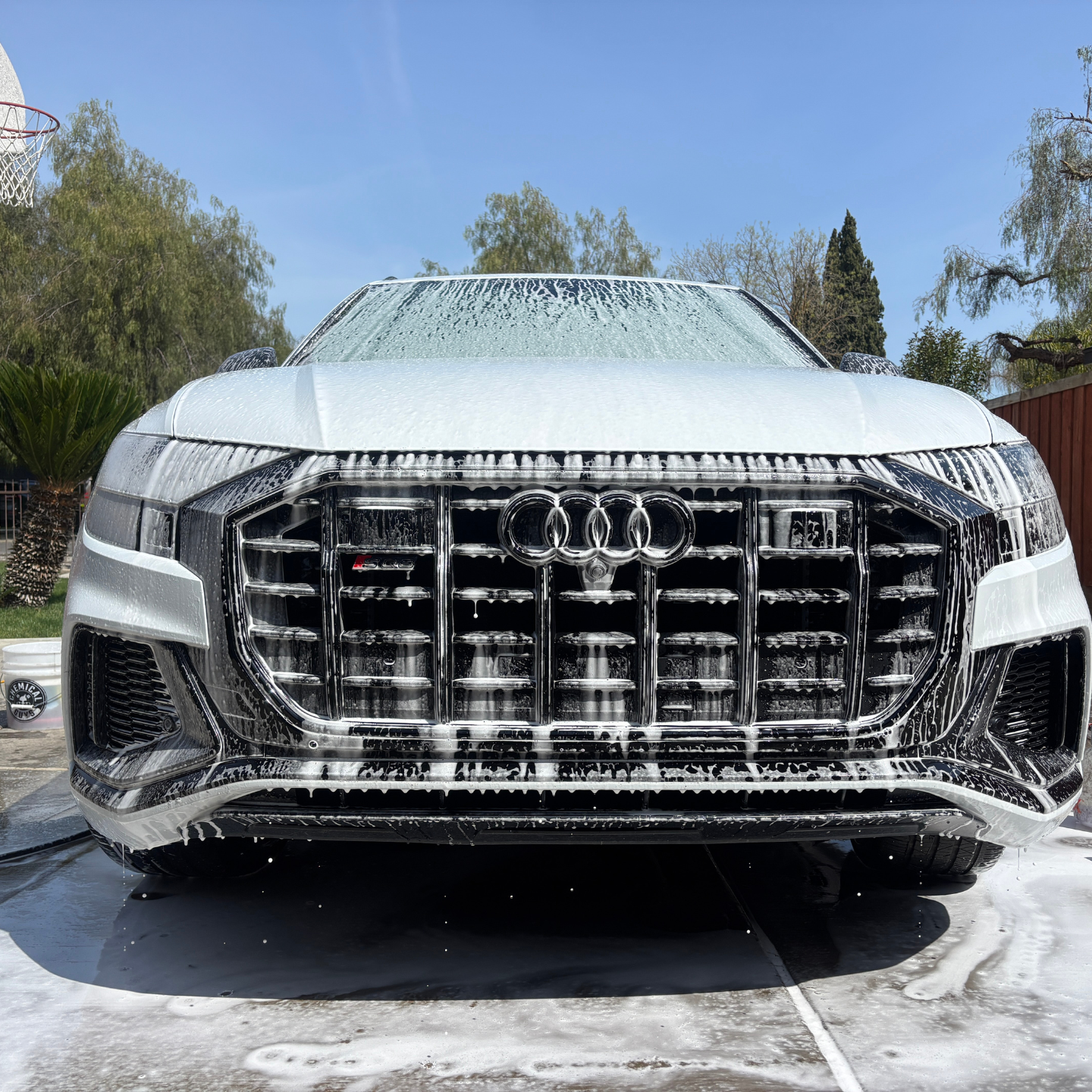 White Audi SUV covered in soap suds, front view in a sunny driveway