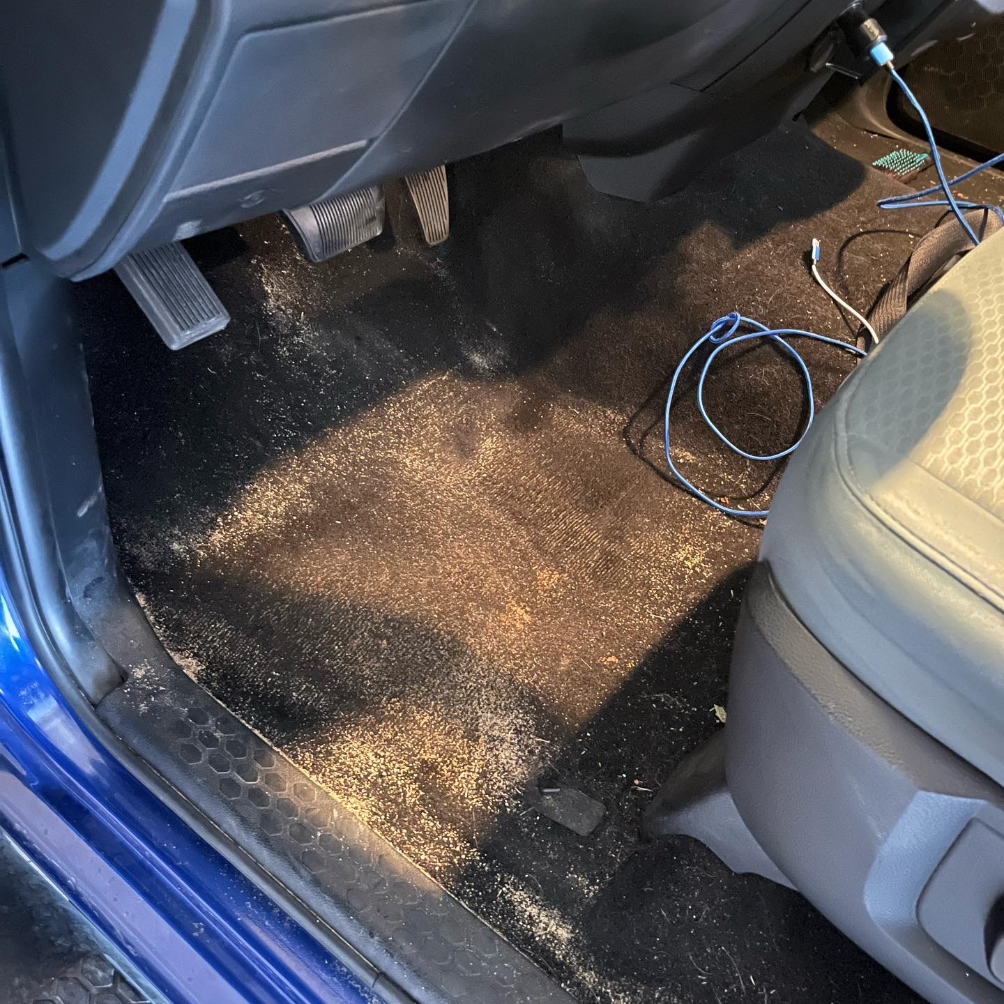 The inside of a blue car with a dirty floor