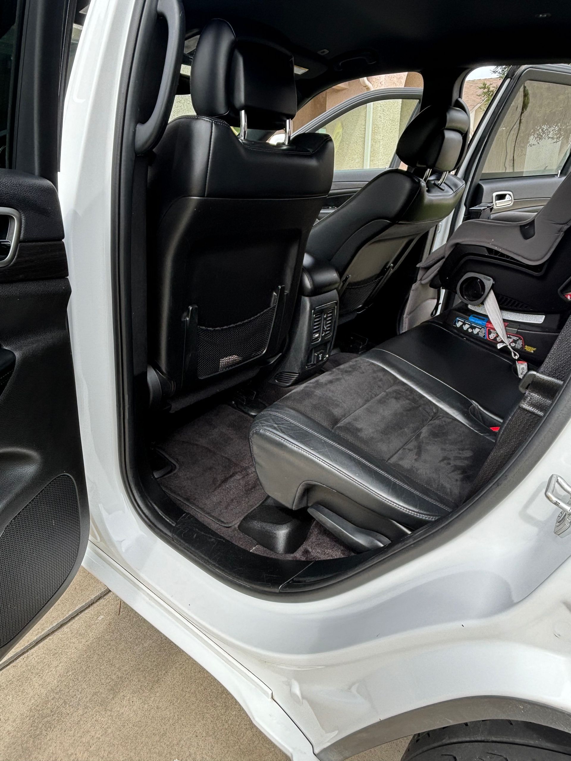 Open car door showing black leather interior and folded rear seat in a silver vehicle