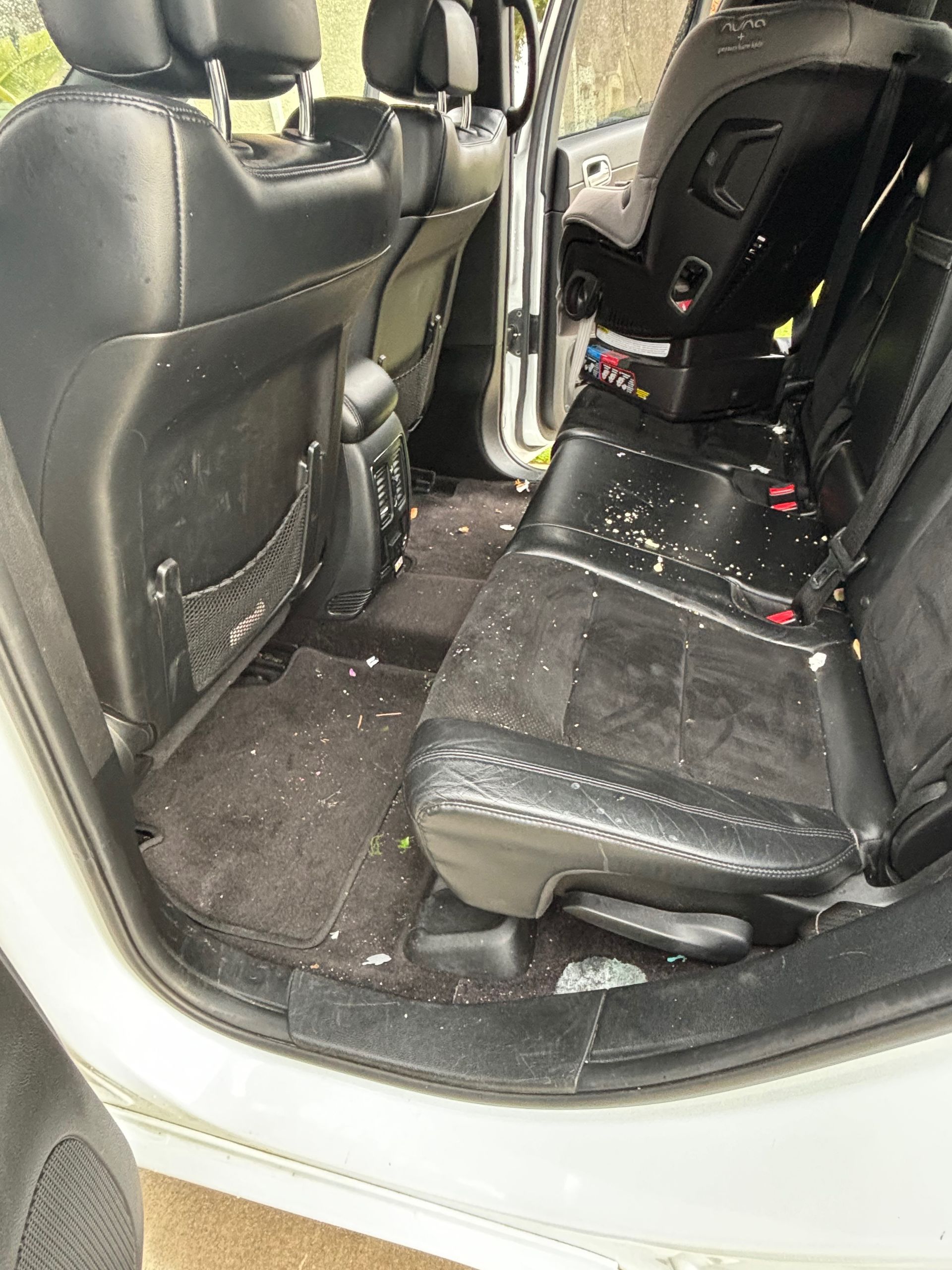 Car interior with black seats and a messy back floor scattered with debris
