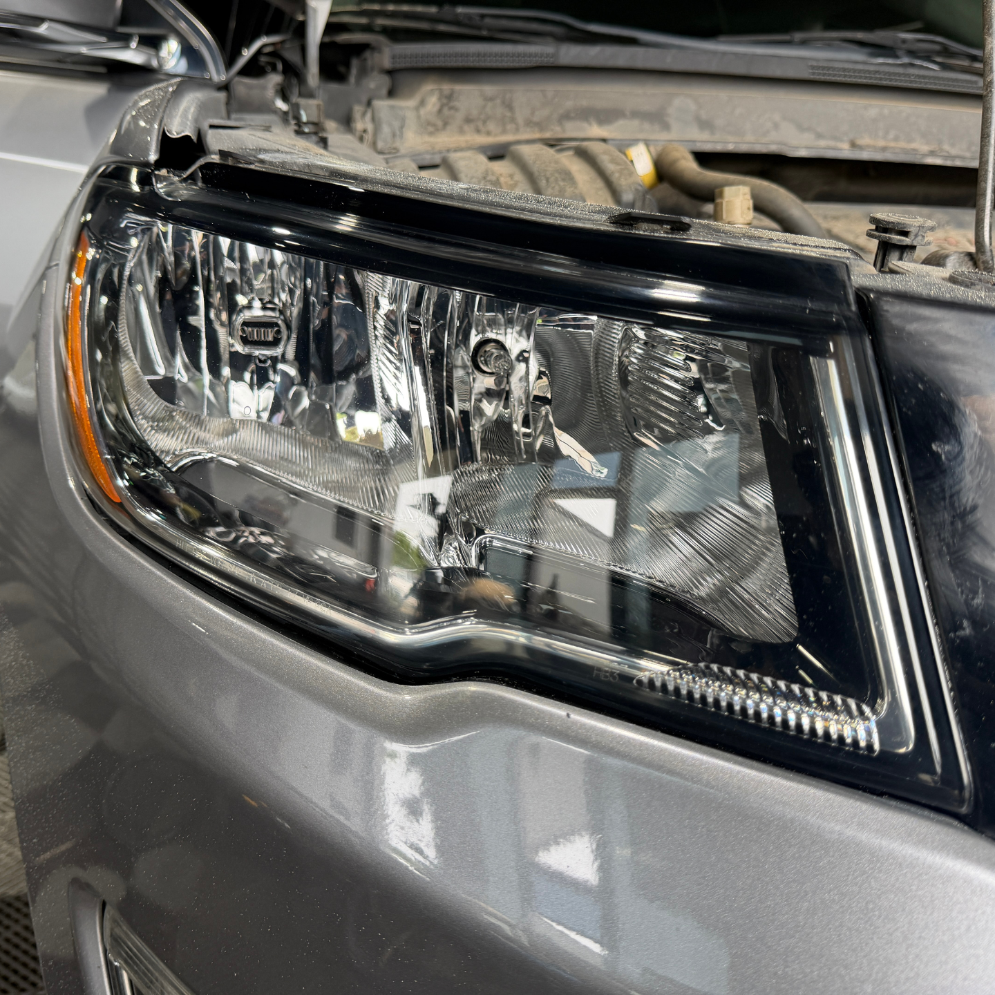 Close-up of a silver car’s headlight assembly with a clear lens and chrome details.