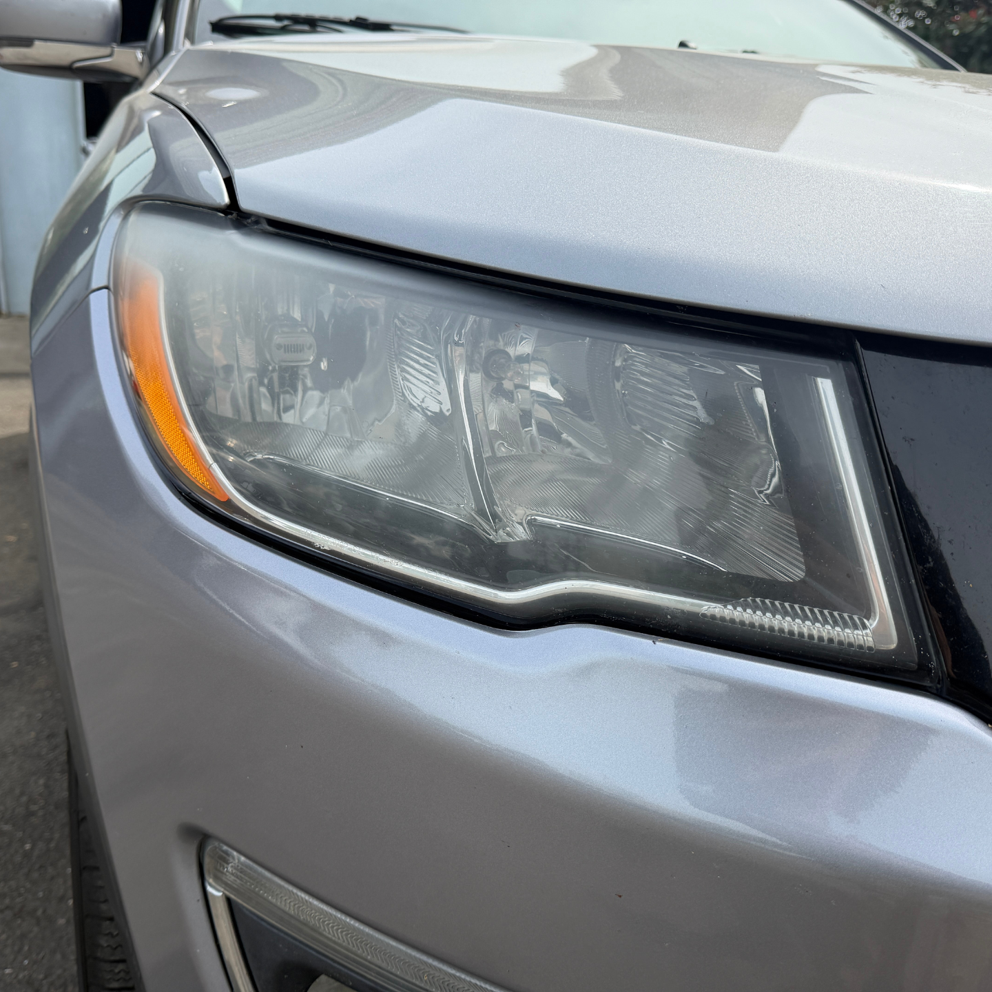 Close-up of a gray car’s front headlight and hood with an orange side marker.