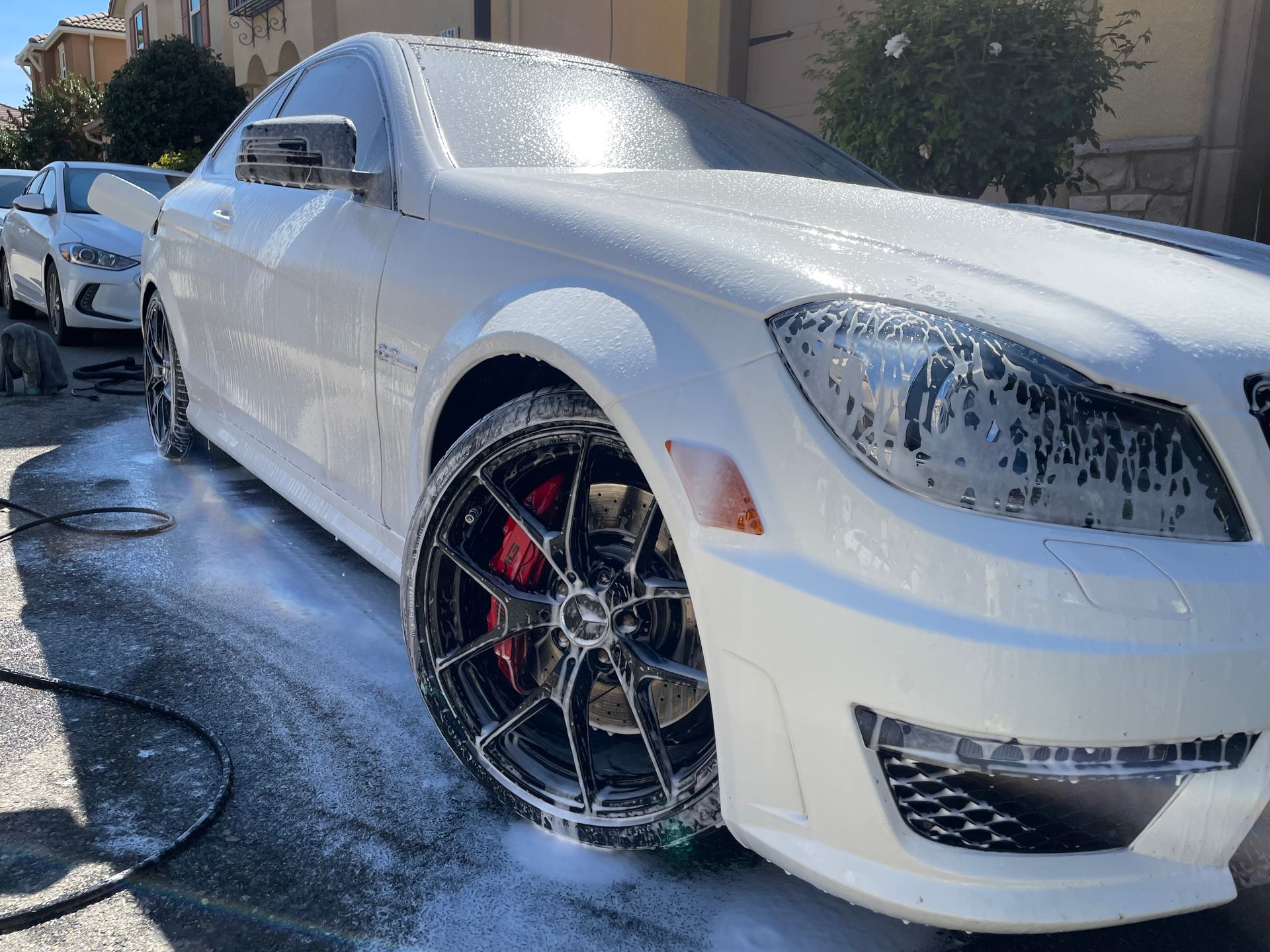 White luxury sedan being washed outdoors with water spraying over the front wheel and hood