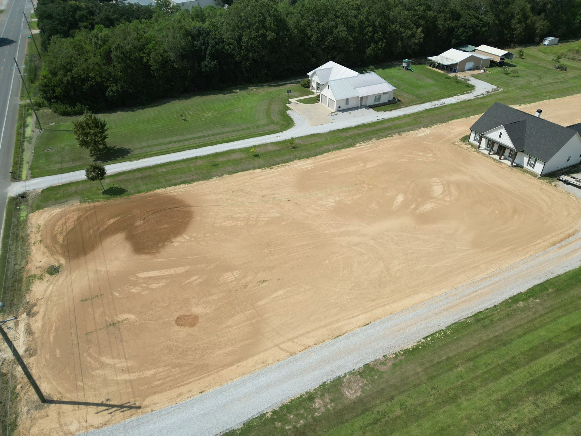 Aerial view of a large sand volleyball court beside a house and trees