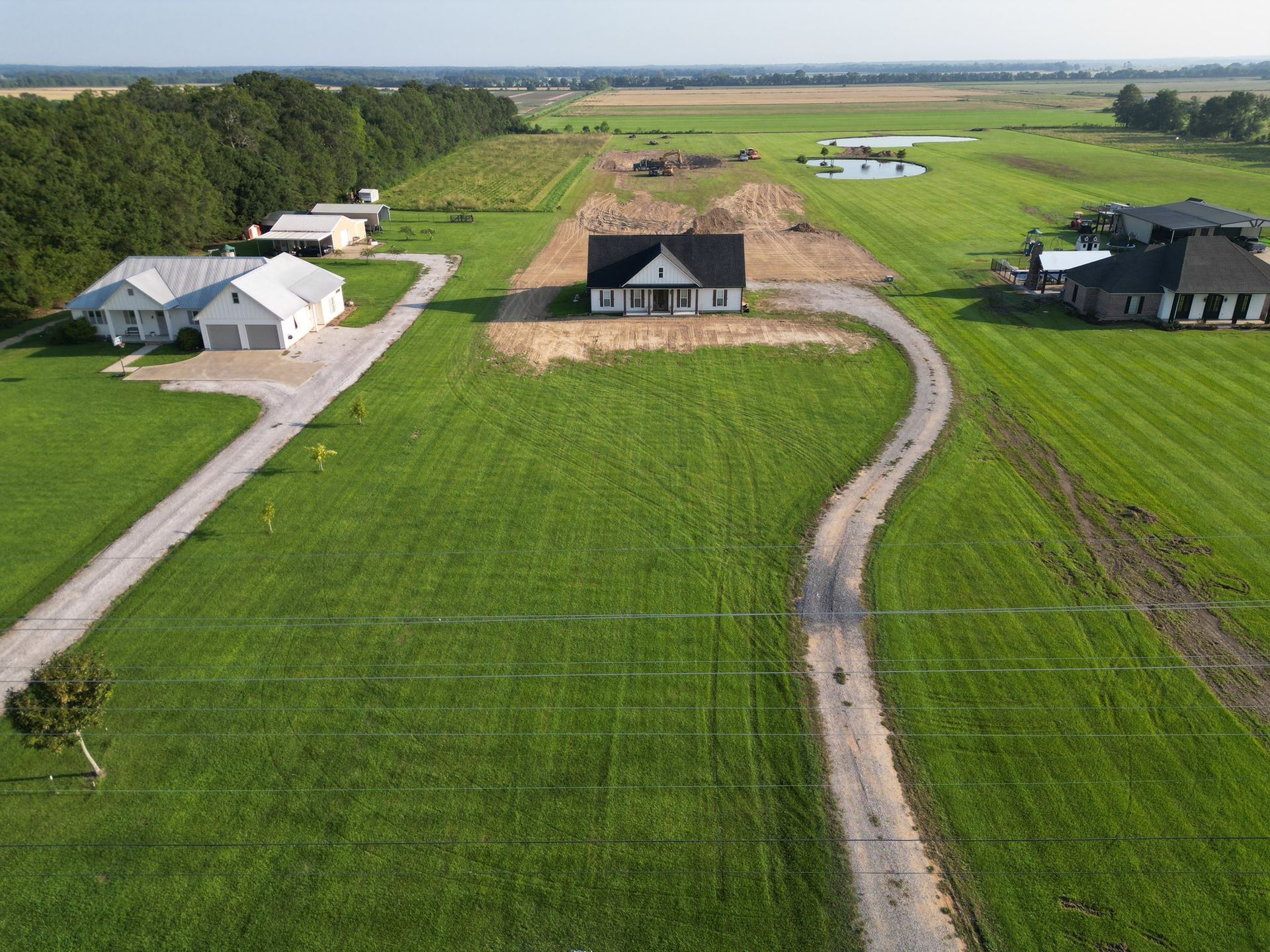 Aerial view of a rural neighborhood with three houses, green fields, and winding dirt roads.