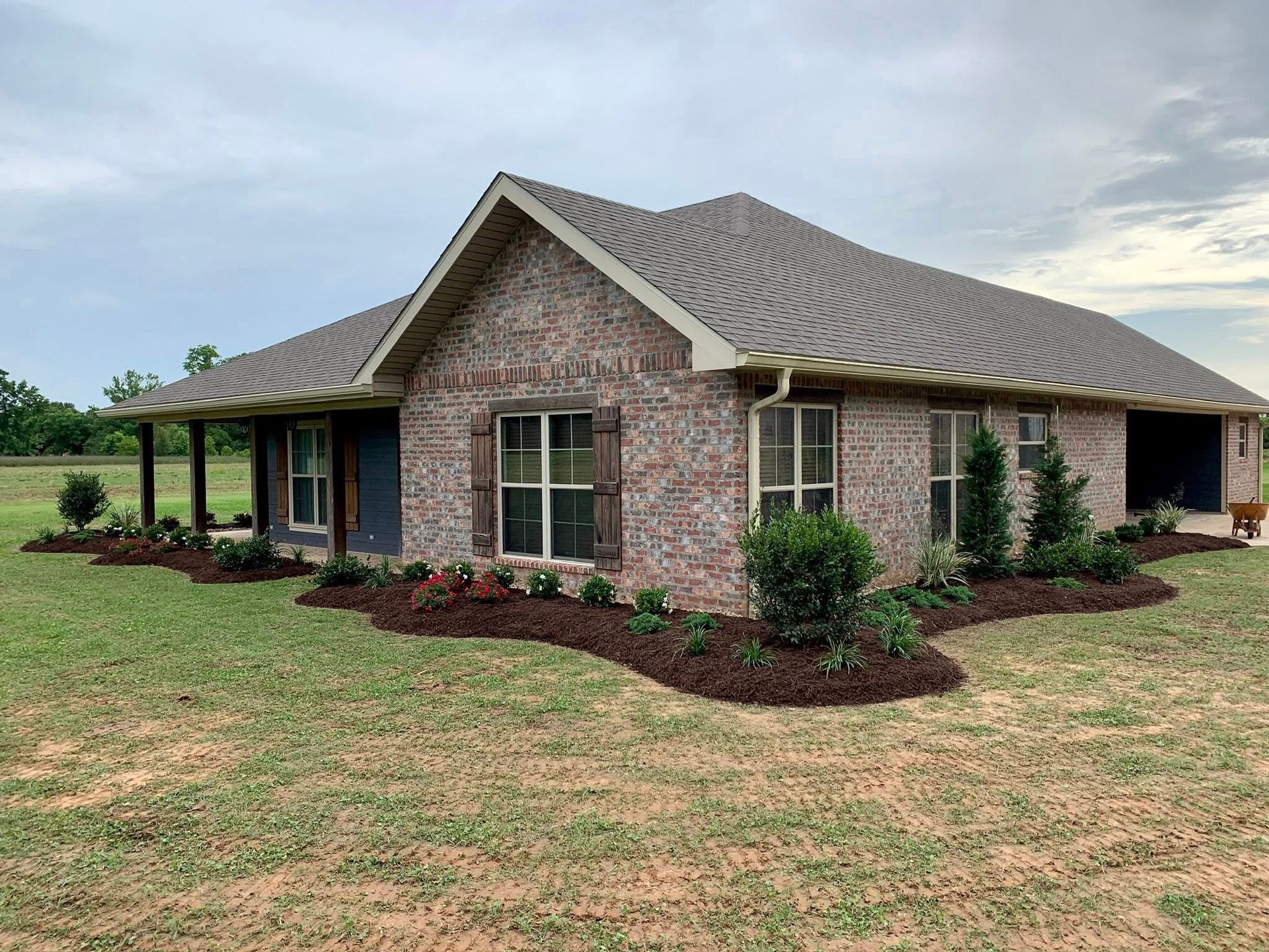 Single-story brick house with a gabled roof, front porch, and landscaped yard under a cloudy sky