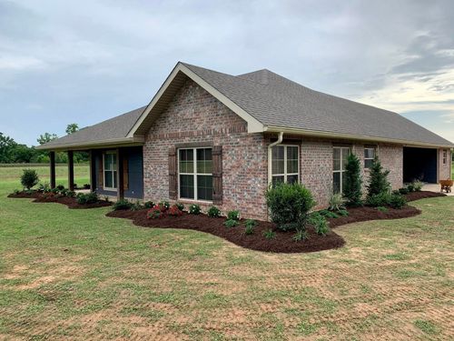 Single-story brick house with a gabled roof, front porch, and landscaped yard under a cloudy sky