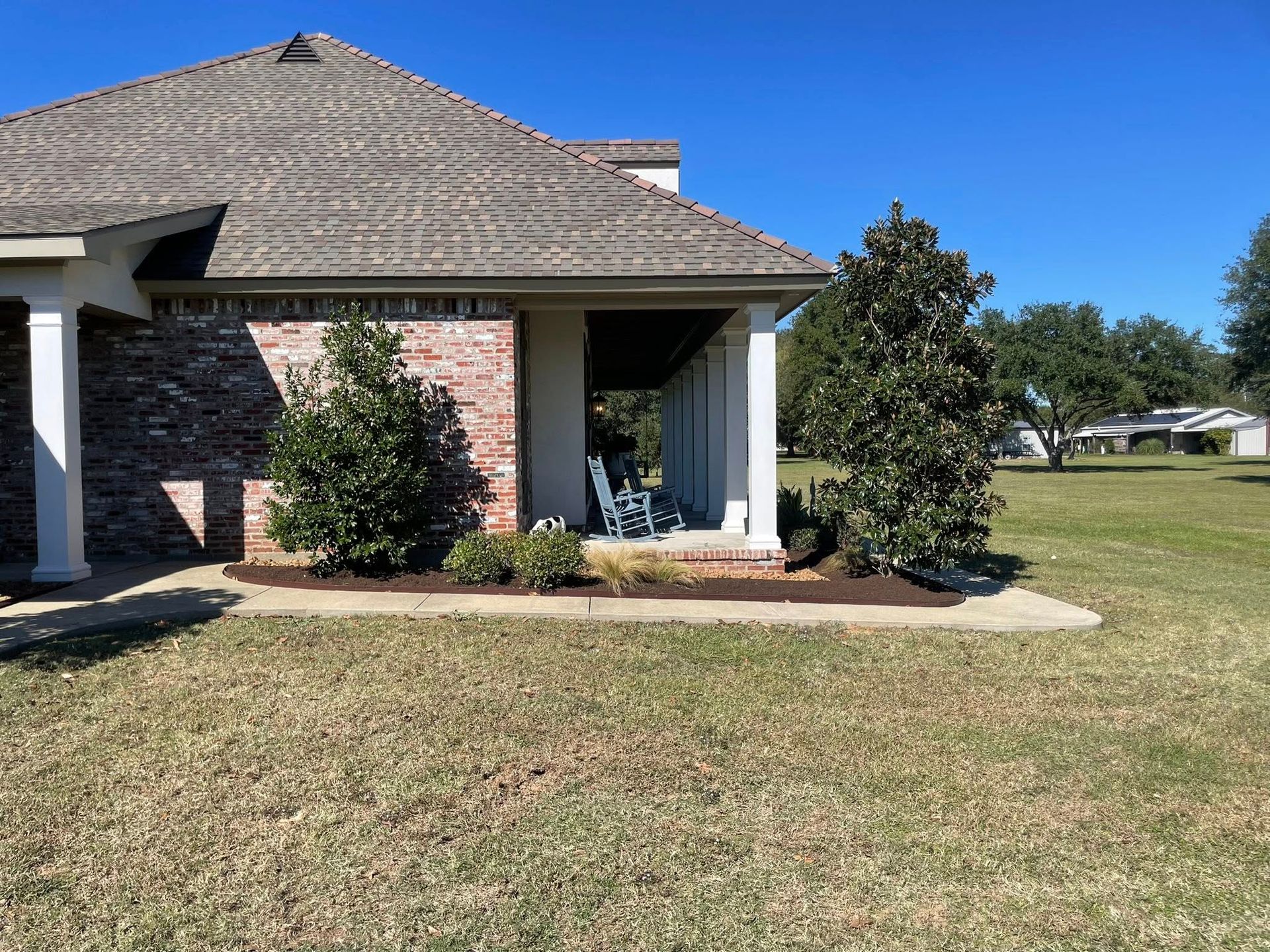 Single-story brick house with a tiled roof and front porch, set on a grassy lawn under a clear blue sky