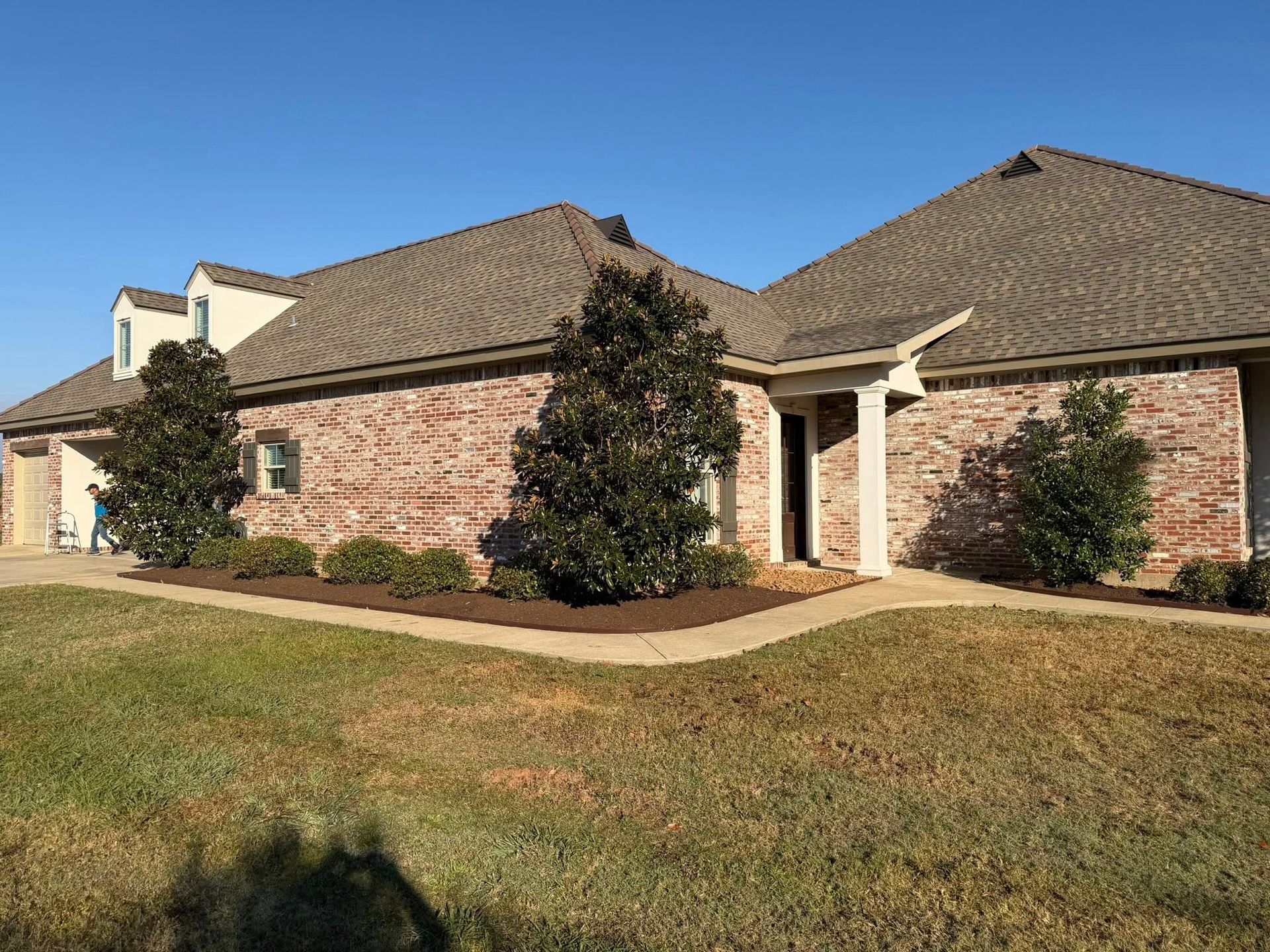 Single-story brick house with tan roof, front walkway, and lawn under a blue sky