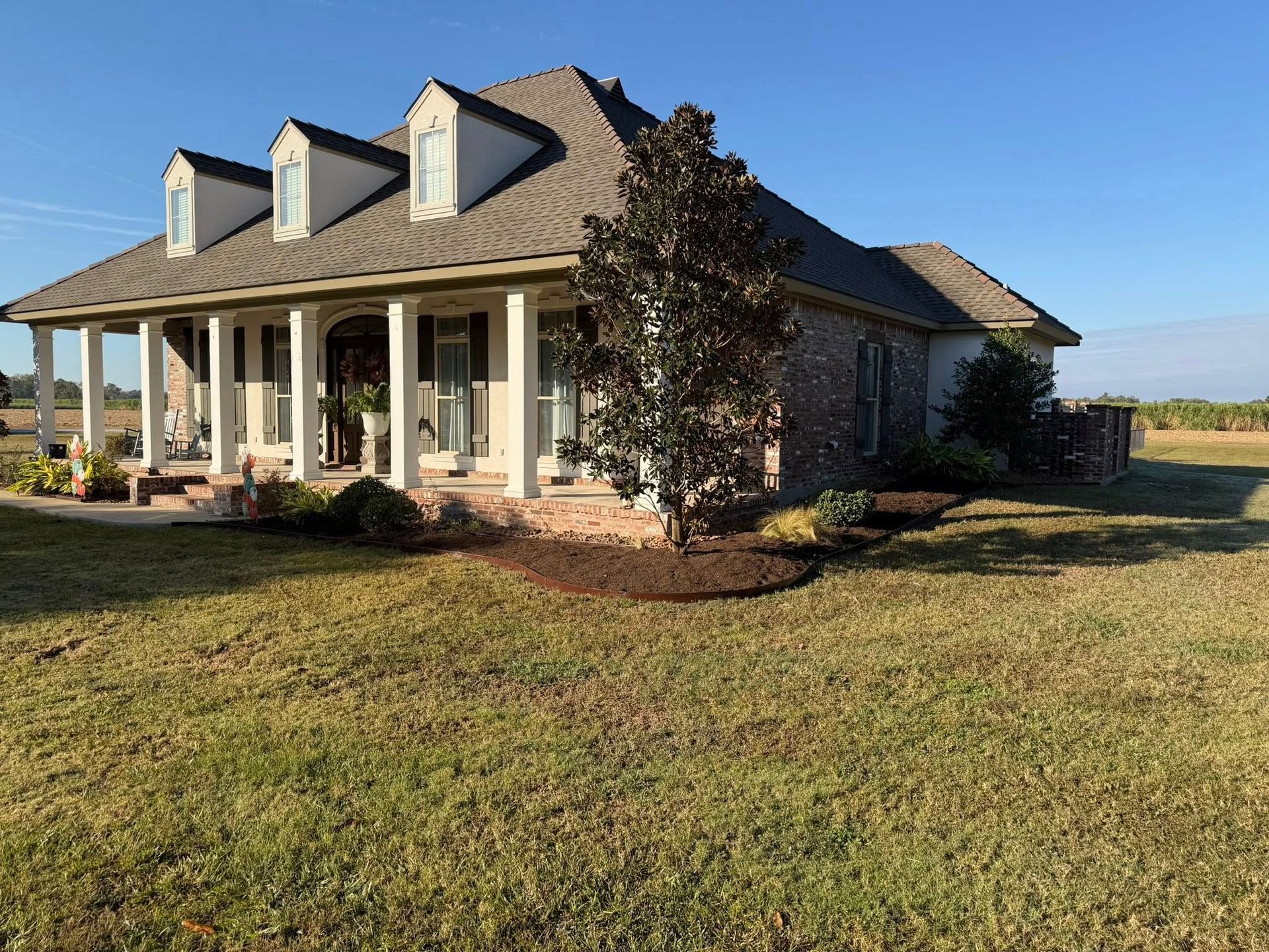 Single-story brick house with a covered porch, dormer windows, and a large grassy yard.