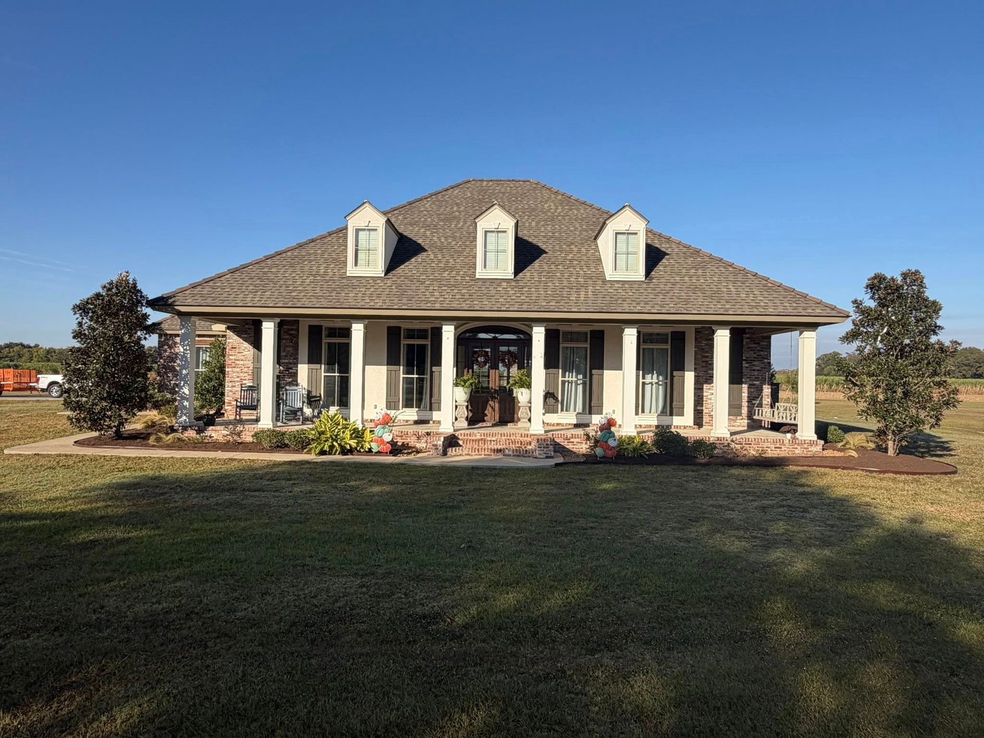 Single-story house with white columns, gray roof, and a wide front porch on a grassy lot