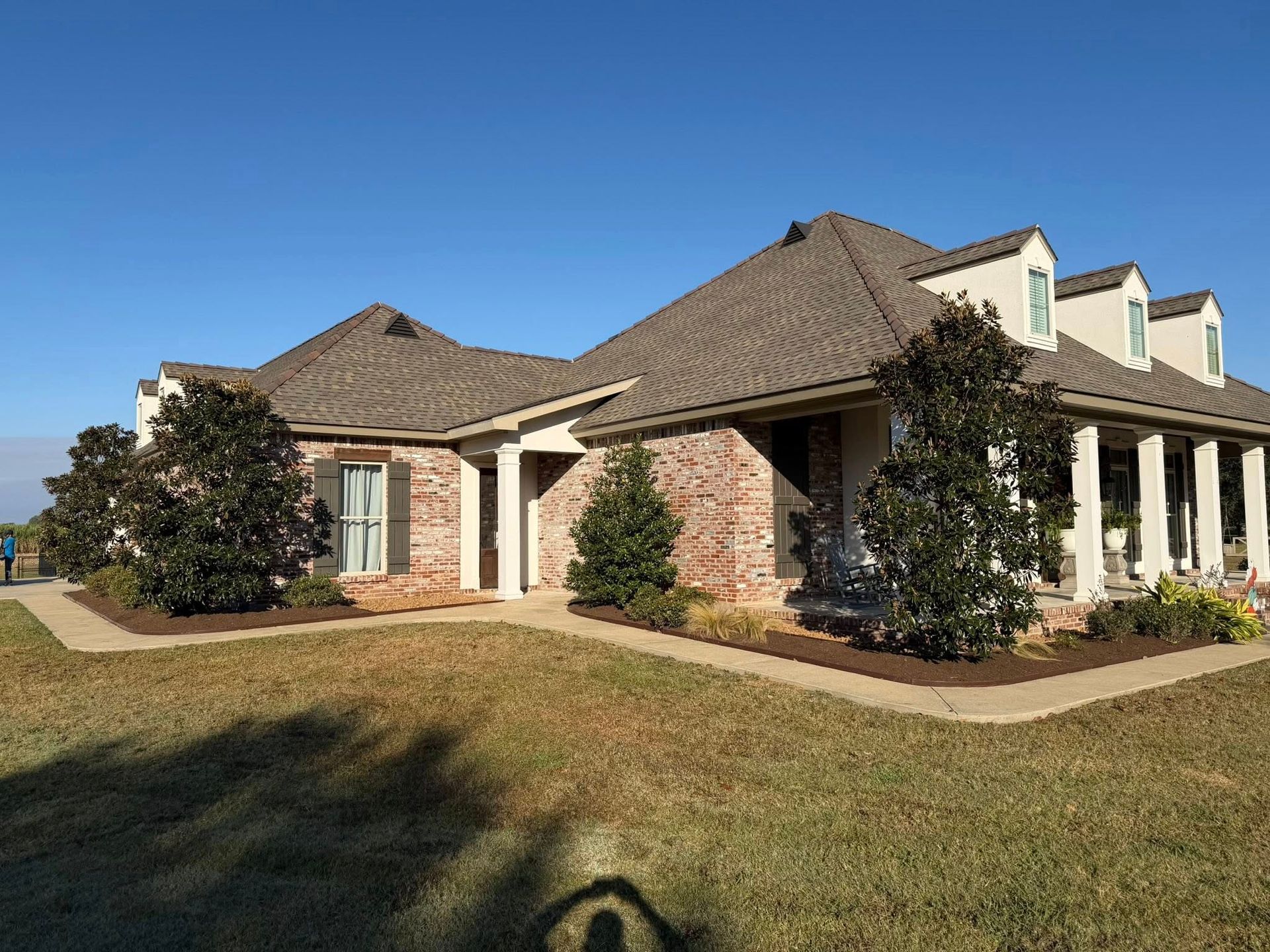 Large single-story brick house with a tiled roof and front lawn under a clear blue sky