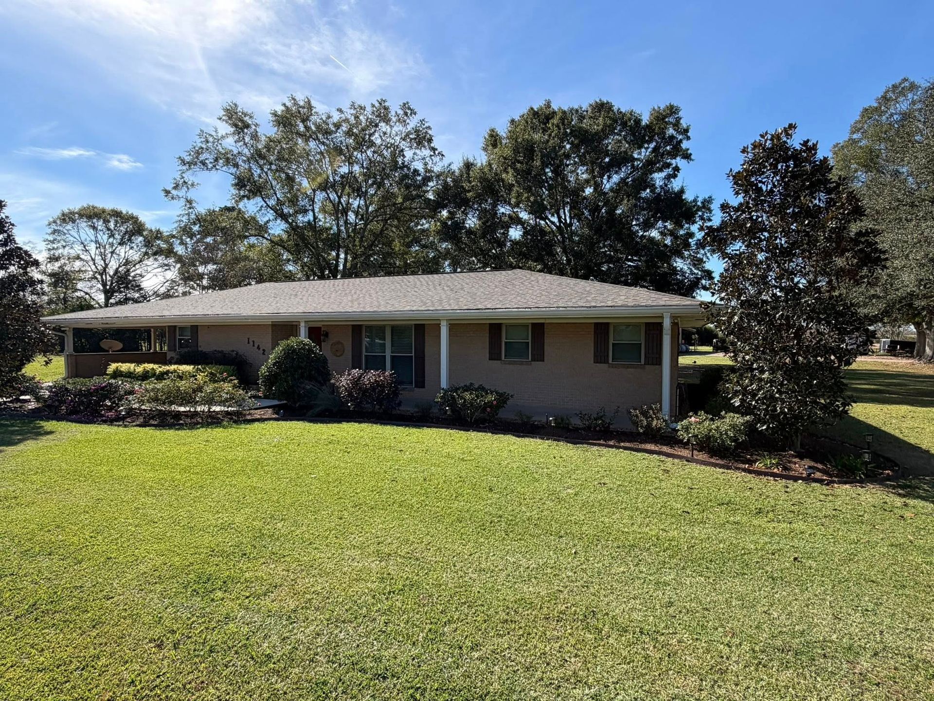 Single-story house with a large front lawn, trees, and a clear blue sky