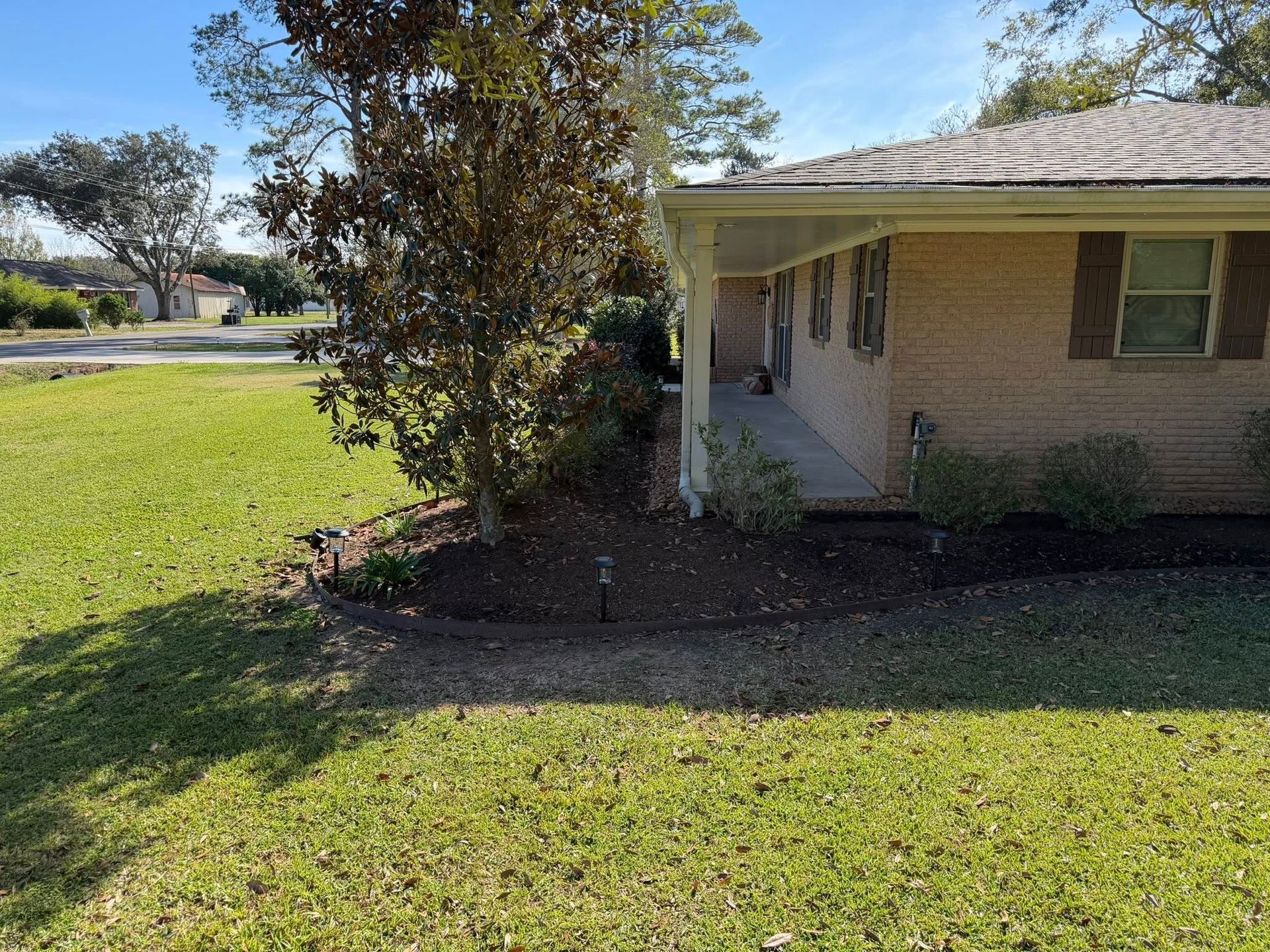 Single-story brick house with a small porch and large tree in the front yard.