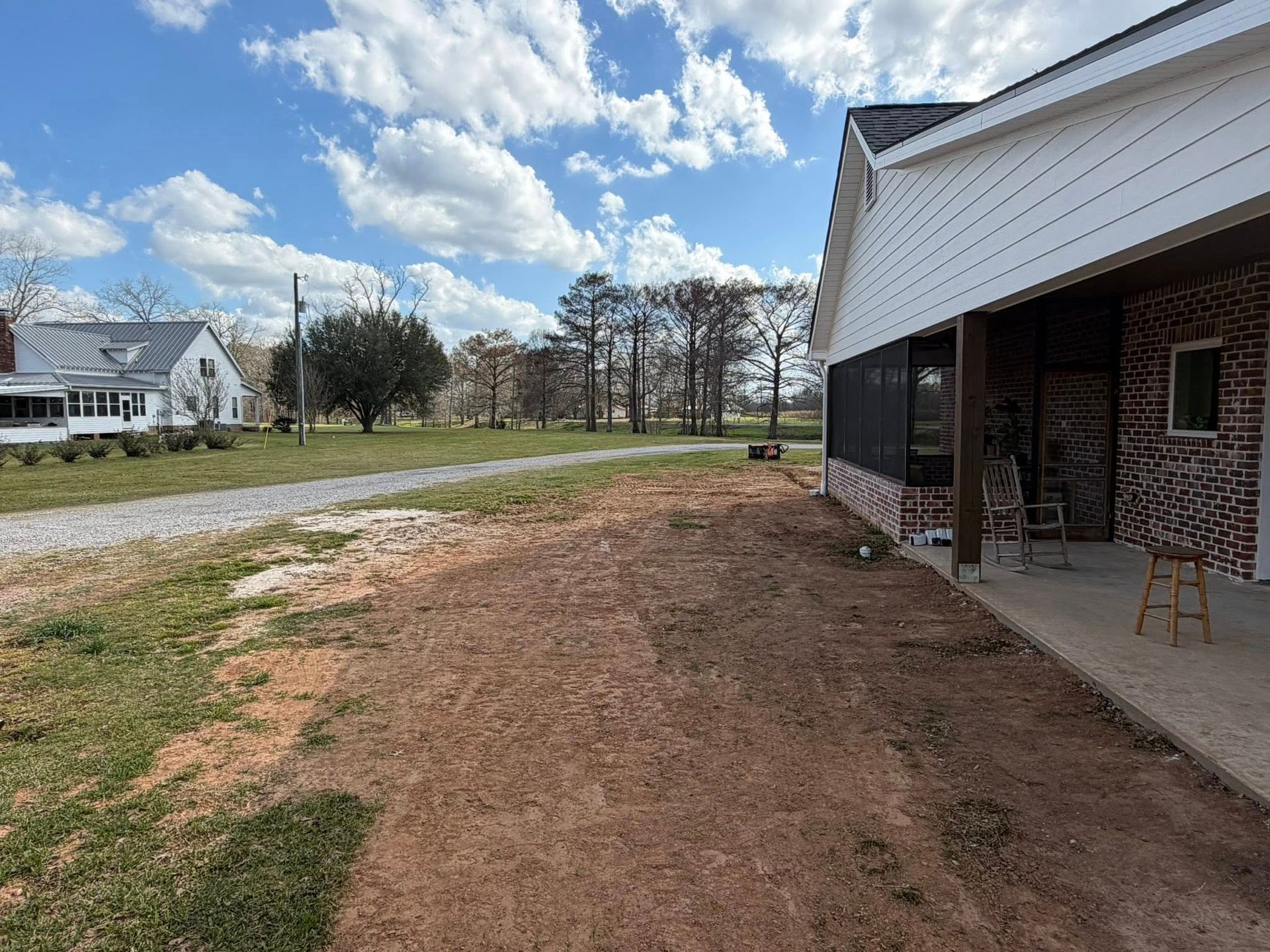Covered porch beside brick building and dirt path leading to a gravel road under a cloudy sky.